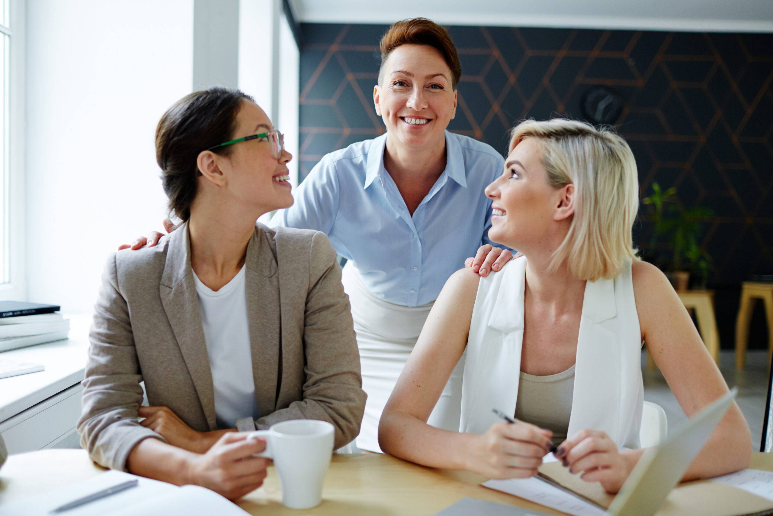 Woman with executive presence addressing two other business women over their shoulders.
