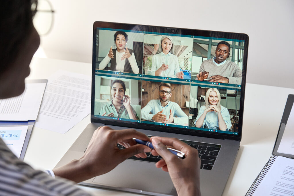 Black woman manager leader having team chat virtual meeting group video conference call with diverse business people remote working online at home office. Teleconference concept. Over shoulder view