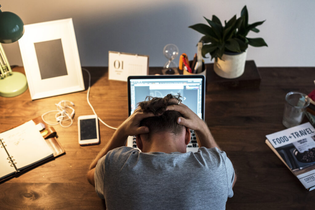 Man experiencing burnout and stress while working remotely on a laptop in a home office setting